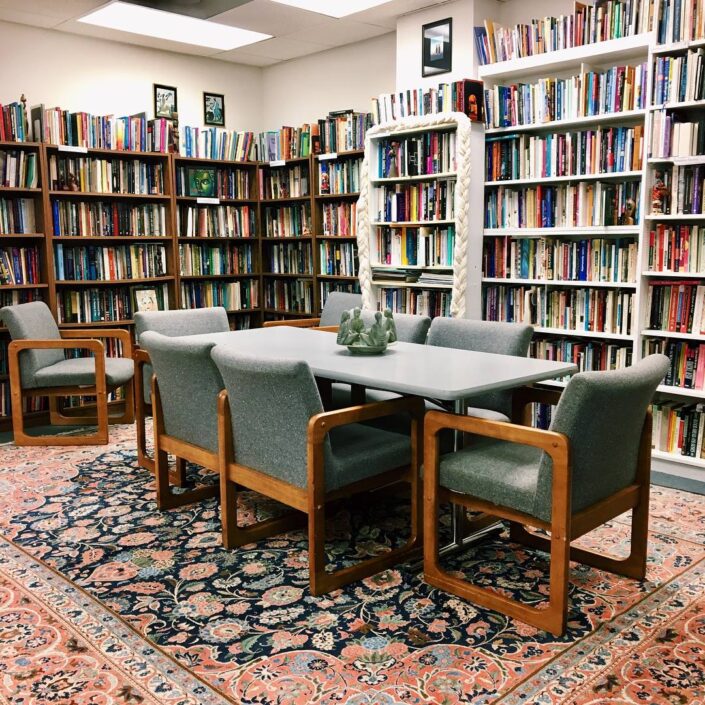 A photo of the WATER office, with a table surround by chairs on a patterned carpet and the walls are wall-to-wall filled bookshelves